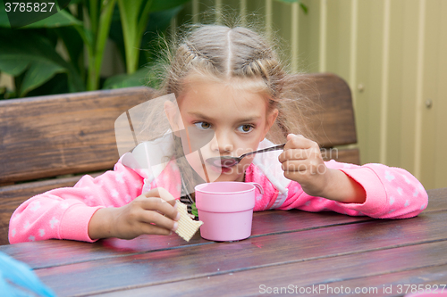 Image of Six-year girl drinks tea from a spoon breakfast on the veranda
