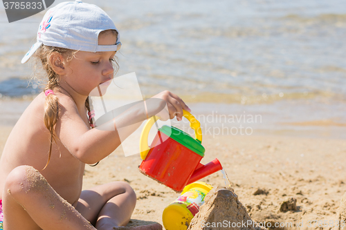 Image of Four-year girl pouring water on sand castle