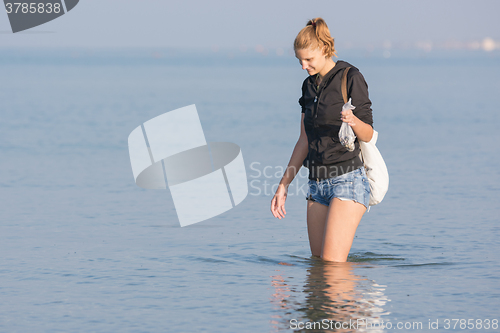Image of A girl walks along the beach and collect shells in the sea early in the morning