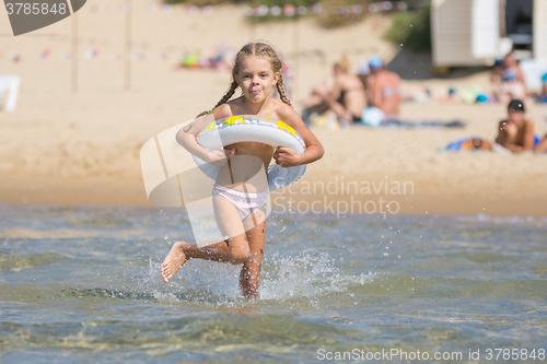 Image of Six-year girl runs with a swimming circle swim in the sea