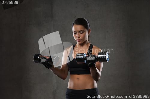 Image of young woman flexing muscles with dumbbells in gym