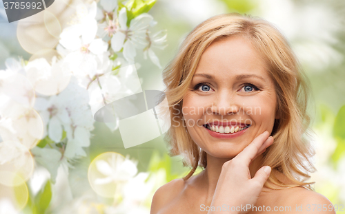 Image of smiling woman with bare shoulders touching face