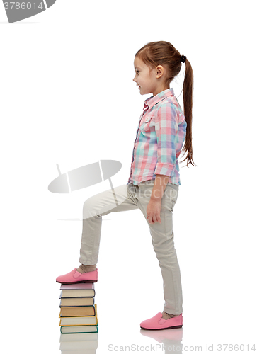 Image of happy little girl stepping on book pile