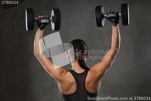 Image of young woman flexing muscles with dumbbells in gym