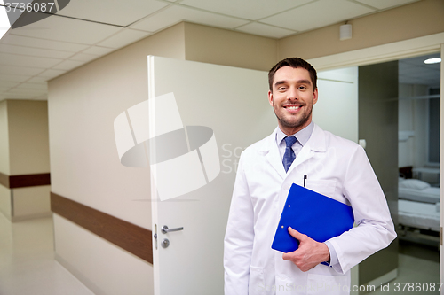 Image of happy doctor with clipboard at hospital corridor