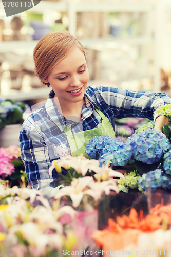 Image of happy woman taking care of flowers in greenhouse