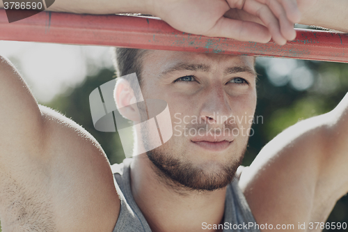 Image of young man exercising on horizontal bar outdoors