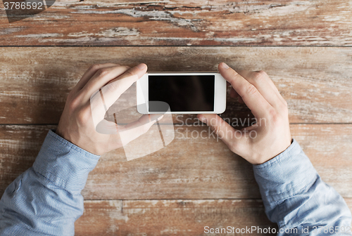 Image of close up of male hands with smartphone on table