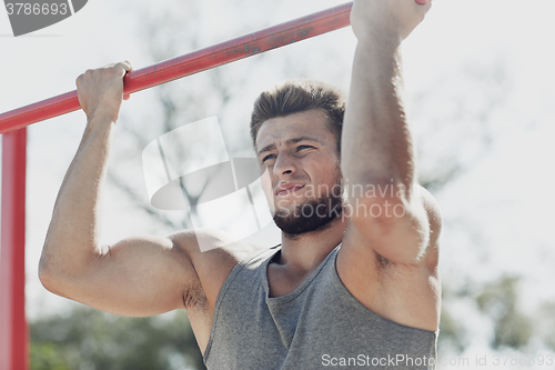 Image of young man exercising on horizontal bar outdoors