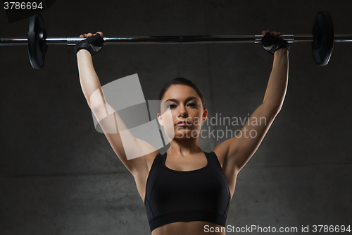 Image of young woman flexing muscles with barbell in gym