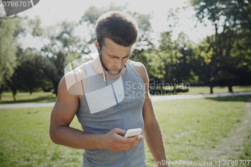 Image of young man with earphones and smartphone at park