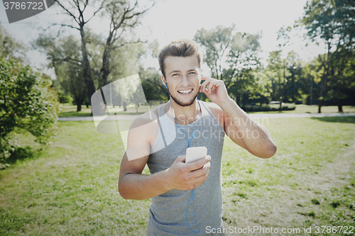 Image of happy man with earphones and smartphone at park