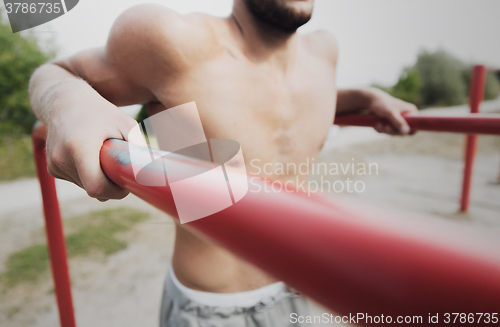 Image of young man exercising on parallel bars outdoors