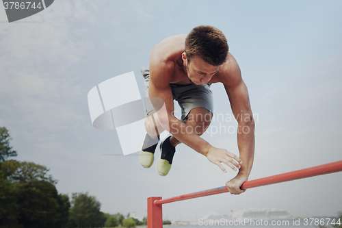 Image of young man exercising on horizontal bar outdoors