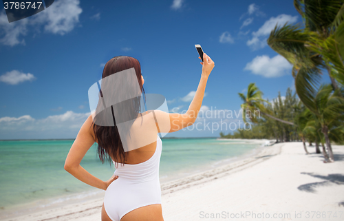 Image of young woman taking selfie with smartphone on beach