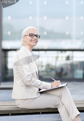 Image of young smiling businesswoman with notepad outdoors