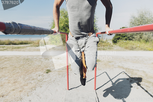 Image of young man exercising on parallel bars outdoors