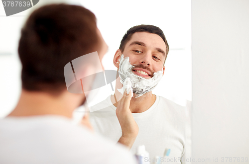 Image of happy man applying shaving foam at bathroom mirror