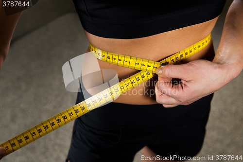 Image of close up of woman measuring waist by tape in gym