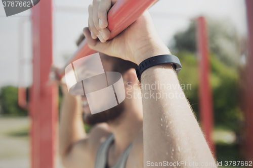 Image of young man exercising on horizontal bar outdoors