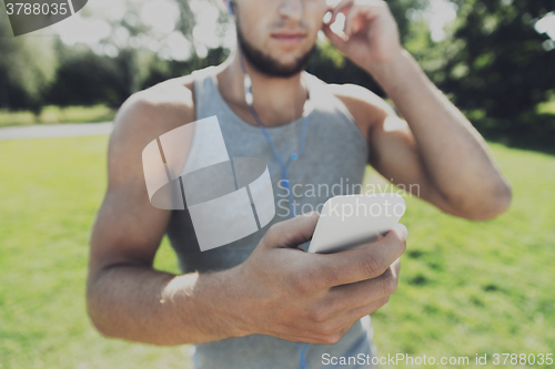 Image of young man with earphones and smartphone at park