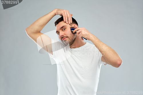 Image of smiling man shaving beard with trimmer over gray