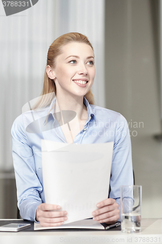 Image of smiling woman holding papers in office