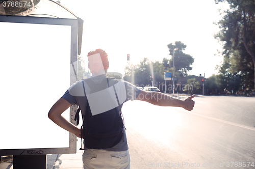 Image of Man standing near bus stop thumbing a lift