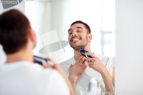 Image of man shaving beard with trimmer at bathroom