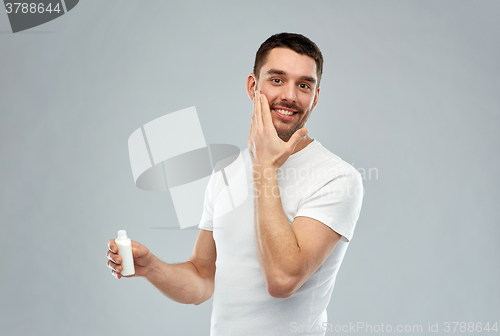 Image of happy young man applying cream or lotion to face