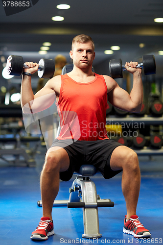 Image of young man with dumbbells flexing muscles in gym