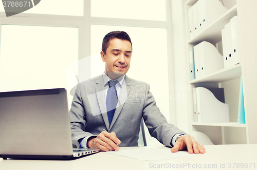 Image of smiling businessman with laptop and papers