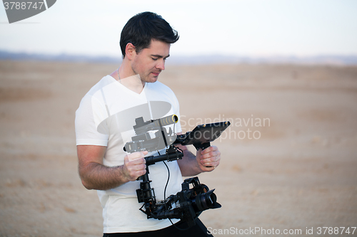 Image of Young man using steadycam for shooting on beach