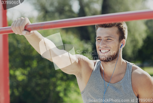 Image of happy young man with earphones and horizontal bar