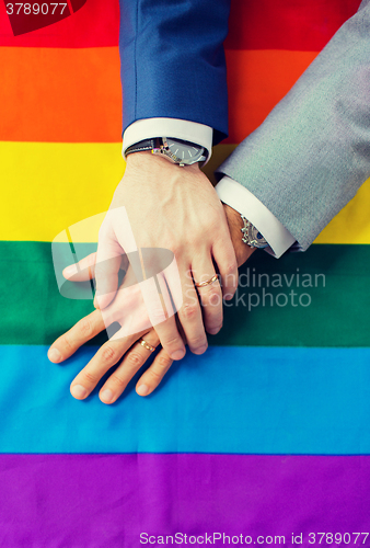 Image of close up of male gay couple hands on rainbow flag