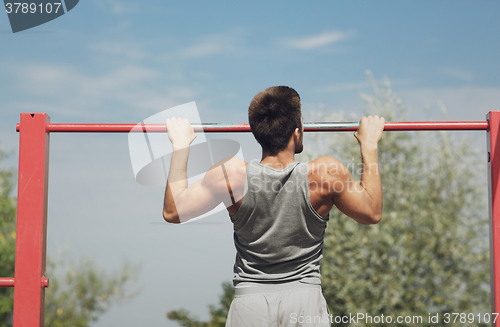 Image of young man exercising on horizontal bar outdoors