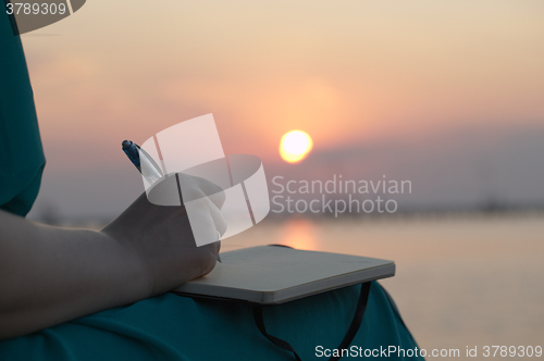 Image of Woman writing in her diary at sunset