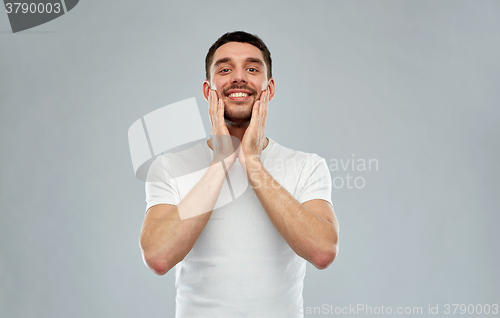 Image of happy young man applying aftershave to face