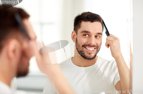 Image of happy man brushing hair  with comb at bathroom