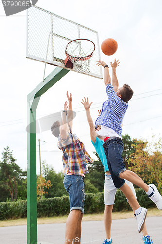 Image of group of happy teenage friends playing basketball