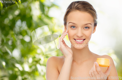 Image of happy young woman applying cream to her face