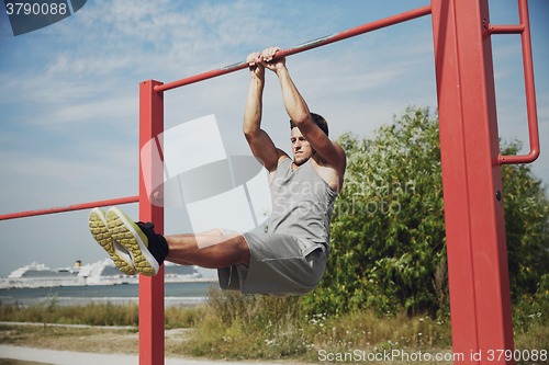 Image of young man exercising on horizontal bar outdoors