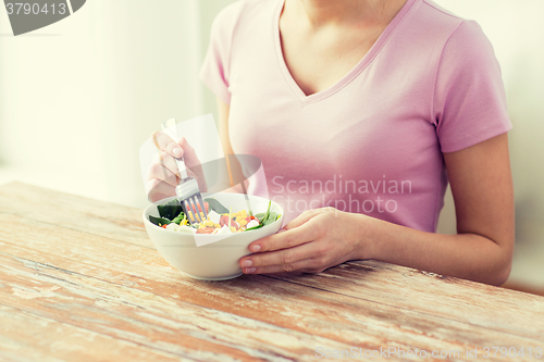 Image of close up of young woman eating salad at home