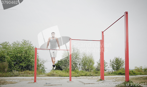 Image of young man exercising on horizontal bar outdoors