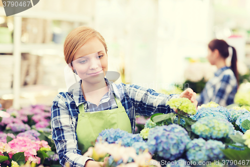 Image of happy woman taking care of flowers in greenhouse