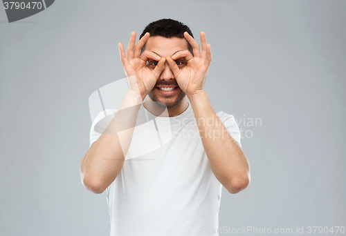 Image of man making finger glasses over gray background
