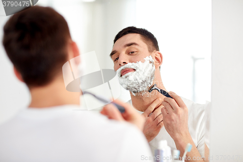 Image of man shaving beard with razor blade at bathroom