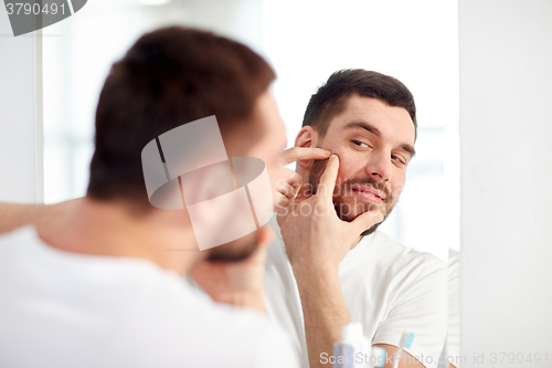 Image of man squeezing pimple at bathroom mirror