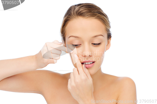 Image of young woman squeezing pimple on her face