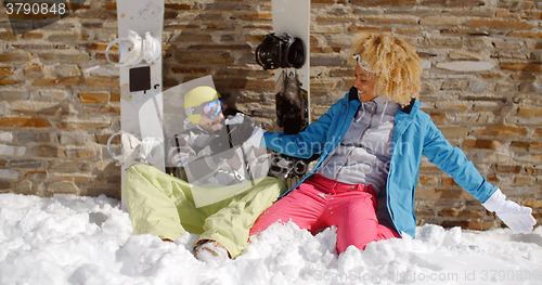 Image of Laughing woman sitting next to friend in snow